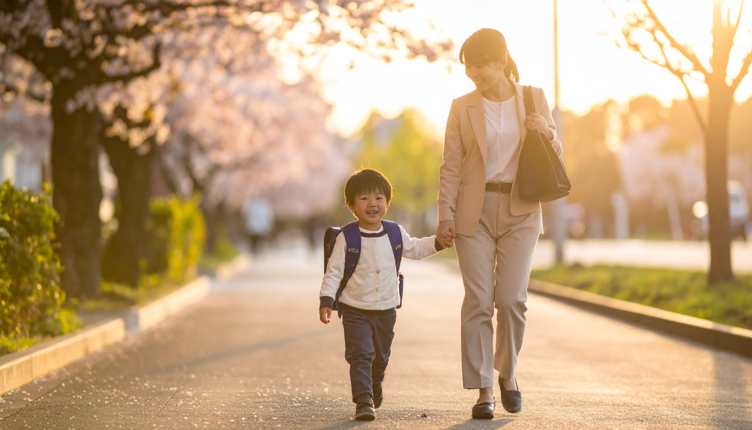 <img src="画像URL" alt="保育園の帰り道、日本人の母親と3歳の男の子が手をつないで笑顔で歩いている様子。" />
